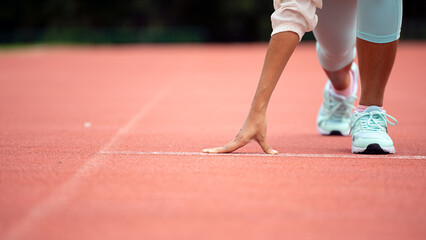 Athlete in starting position on running track, wearing light blue athletic shoes and white leggings, preparation and determination before race