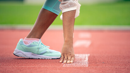 Close-up of athlete in starting position on track, wearing light blue running shoes and white socks, focus on hand and foot placement