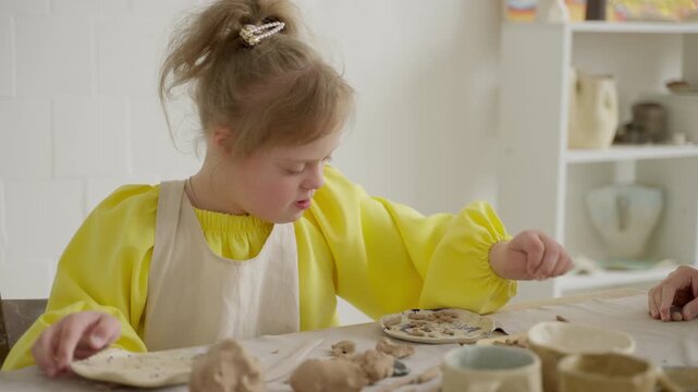Child with Down syndrome participates in clay workshop, focused on her craft. Moment underscores the importance of art education, developmental support. Concept: developmental growth, art skills.
