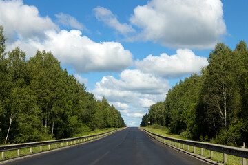 A Beautiful Scenic Open Road Stretching Under a Bright Blue Sky with Fluffy White Clouds