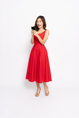 Happy Young Asian woman in red dress standing and using mobile phone isolated on white background, Full body composition