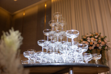 A tall stack of champagne glasses with a floral arrangement in the background