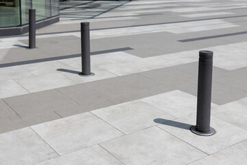 Three black poles are standing in a row on a gray and white sidewalk