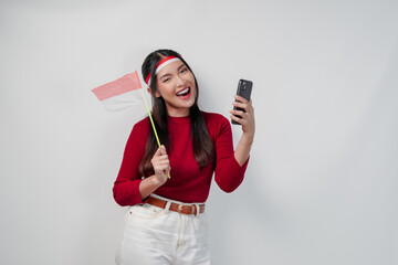 Excited young Asian woman holding Indonesian mini flag smiling while using her cell phone.