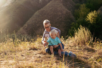 Mother and her son playing outdoors in nature in summer sitting on grass with sun rays on sunset