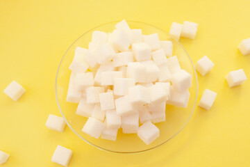 White sugar cubes on glass plate on yellow color background, sweet ingredient