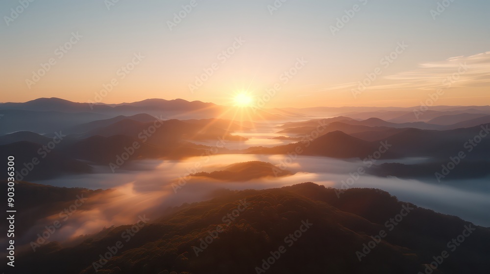 Aufkleber The sun is setting over a mountain range, casting a warm glow over the landscape. The sky is filled with clouds, creating a sense of calm and serenity. The mountains are covered in trees