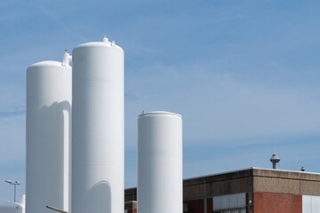 Tall white storage tanks stand prominently against a clear blue sky near an industrial building, highlighting the facility's storage capabilities.