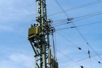 Workers perform maintenance on a high voltage transmission tower against a clear blue sky.