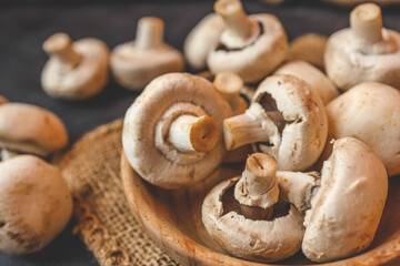 Champignon mushrooms in a wooden plate on a dark background