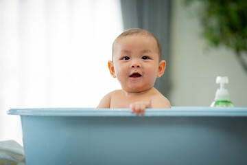 A baby is in a bathtub with a bottle of lotion next to it. The baby is smiling and looking at the camera