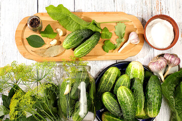 Fresh cucumbers in a jar, spices, garlic and leaves on a wooden kitchen table, homemade pickling recipe, village harvest, cucumbers and ingredients for pickling, home canning concept.