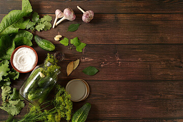 Fresh cucumbers in a jar, spices, garlic and leaves on a wooden kitchen table, homemade pickling recipe, village harvest, cucumbers and ingredients for pickling, home canning concept.