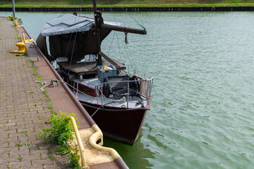 A dld boat rests quietly at the dock, nestled by the canal, with a calm waters.