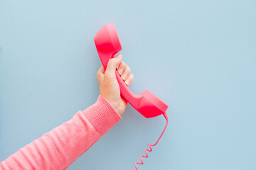 Communication and contact concept - woman hand with pink phone on light blue background