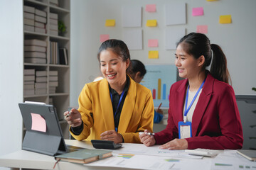 Two young businesswomen smiling and working together using a tablet computer in a modern office