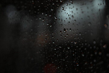 A close-up photo of raindrops on a car window, creating a beautiful abstract pattern against a bokeh-filled backdrop.
