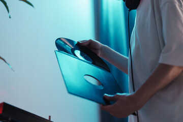DJ examines a vinyl record closely, preparing for a music set with a turntable in view.