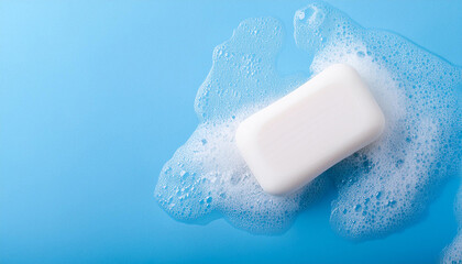 White soap bar and foam on blue background. Skin care and hygiene. Close-up. Flat lay