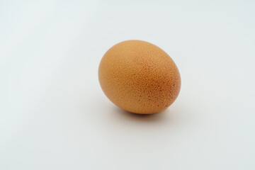 A lone brown egg is positioned on a clean white surface. The shell displays tiny blemishes and a feather, suggesting its organic farm origin. Ideal for preparing nutritious meals and recipes.