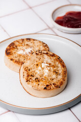 Hot Toasted Crumpets with piece of butter on a plate with strawberry jam nearby. Perfect tasty breakfast