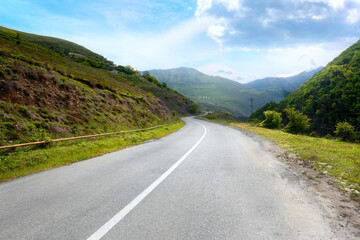 Fototapeta premium Asphalt road in the mountains with a view of the medieval towers of Erzi. Mountains of Ingushetia