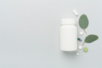 Bottle with pills and green leaves on color background, top view