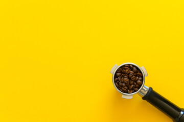 Espresso portafilter with whole coffee beans on a yellow background