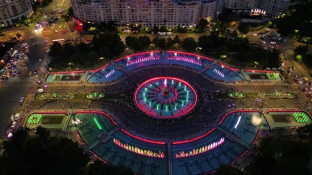 Aerial footage of the light show of the Bucharest fountains on a summer evening. Drone shot of the magnificent lights illuminating the mesmerizing dancing water fountain. Tourist attraction in summer.