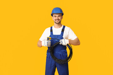 Portrait of male electrician with crimper and wires on yellow background