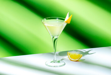 Alcoholic cocktail drink with gin, vodka, aperitif, lemon zest and ice in glass on green background, hard light
