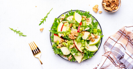Delicious crispy vegan salad with green and red apples, fresh celery, lettuce, arugula and walnuts on plate, white background, top view