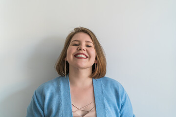 Cheerful plus size young woman with broad smile standing against white plain background. 