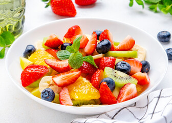 Summer vegan fruity salad with strawberries, blueberries, banana, kiwi, orange and mint on white background, top view