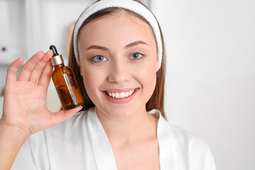 Fototapeta premium Smiling young woman holding amber dropper bottle with skincare serum, beauty routine and facial treatment
