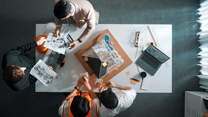 Top view of manager handed blueprint to professional engineer team at meeting table with house model and project plan. Group of architect discussing about design while receive document. Alimentation.