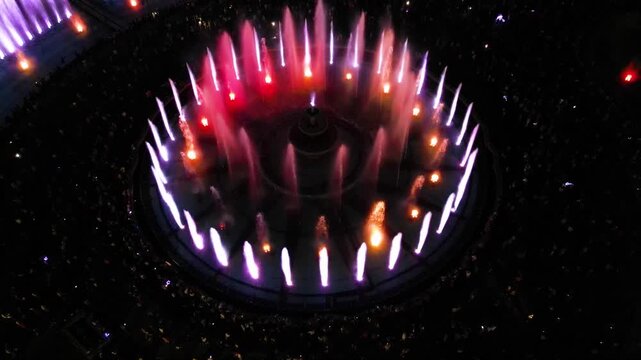 Aerial footage of the light show of the Bucharest fountains on a summer evening. Drone shot of the magnificent lights illuminating the mesmerizing dancing water fountain. Tourist attraction in summer.