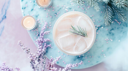 Iced latte with rosemary garnish in a cup | Winter-themed setting with candles and pine branches | Marble surface with lavender and pink decorative elements