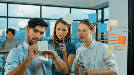 Obraz premium Professional business team brainstorm, sharing, thinking idea while skilled male leader write on sticky notes at glass wall. Skilled manager placed business plan on glass wall at office. Tracery