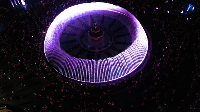 Aerial footage of the light show of the Bucharest fountains on a summer evening. Drone shot of the magnificent lights illuminating the mesmerizing dancing water fountain. Tourist attraction in summer.