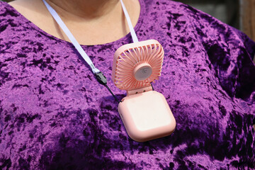 Portable cooling fan close-up, on strap around the neck of an overweight woman