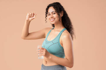 Young African-American woman taking fish oil on beige background