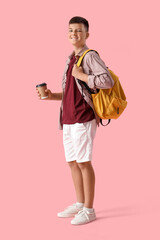 Teenage boy with backpack and cup of coffee on pink background
