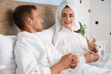 Young couple in bathrobes after shower talking on bed at home