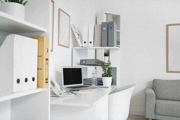 Blank laptop with water bottle and plant on desk in light office