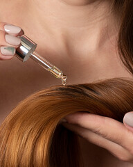 Woman applying serum or oil to ends of hair close-up