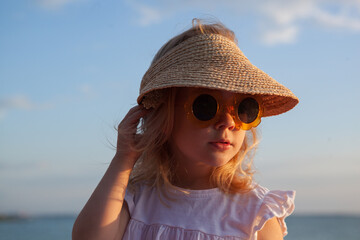 Young child enjoying a summer day at the beach wearing vintage sunglasses and a straw hat