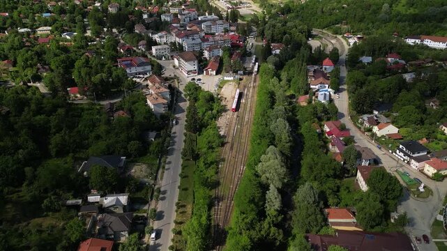 Aerial Drone Footage of a Train Approaching a Quaint Station of Slanic Romania Amidst Lush Trees &ndash; Scenic Journey Through Nature. Transportation concept seen from above. High angle shot.
