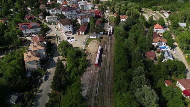 Aerial Drone Footage of a Train Approaching a Quaint Station of Slanic Romania Amidst Lush Trees &ndash; Scenic Journey Through Nature. Transportation concept seen from above. High angle shot.
