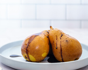 Two whole baked pears in the oven with chocolate syrup in a plate close up.